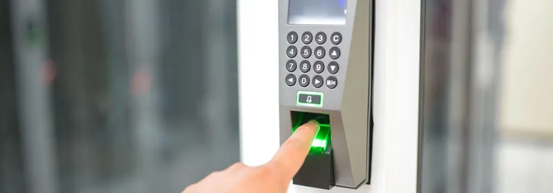 Persona apoyando el dedo en un lector biométrico de huella junto a una puerta